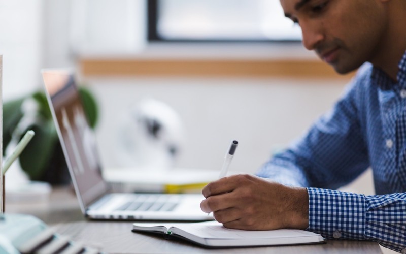 Person sitting at desk with book and laptop